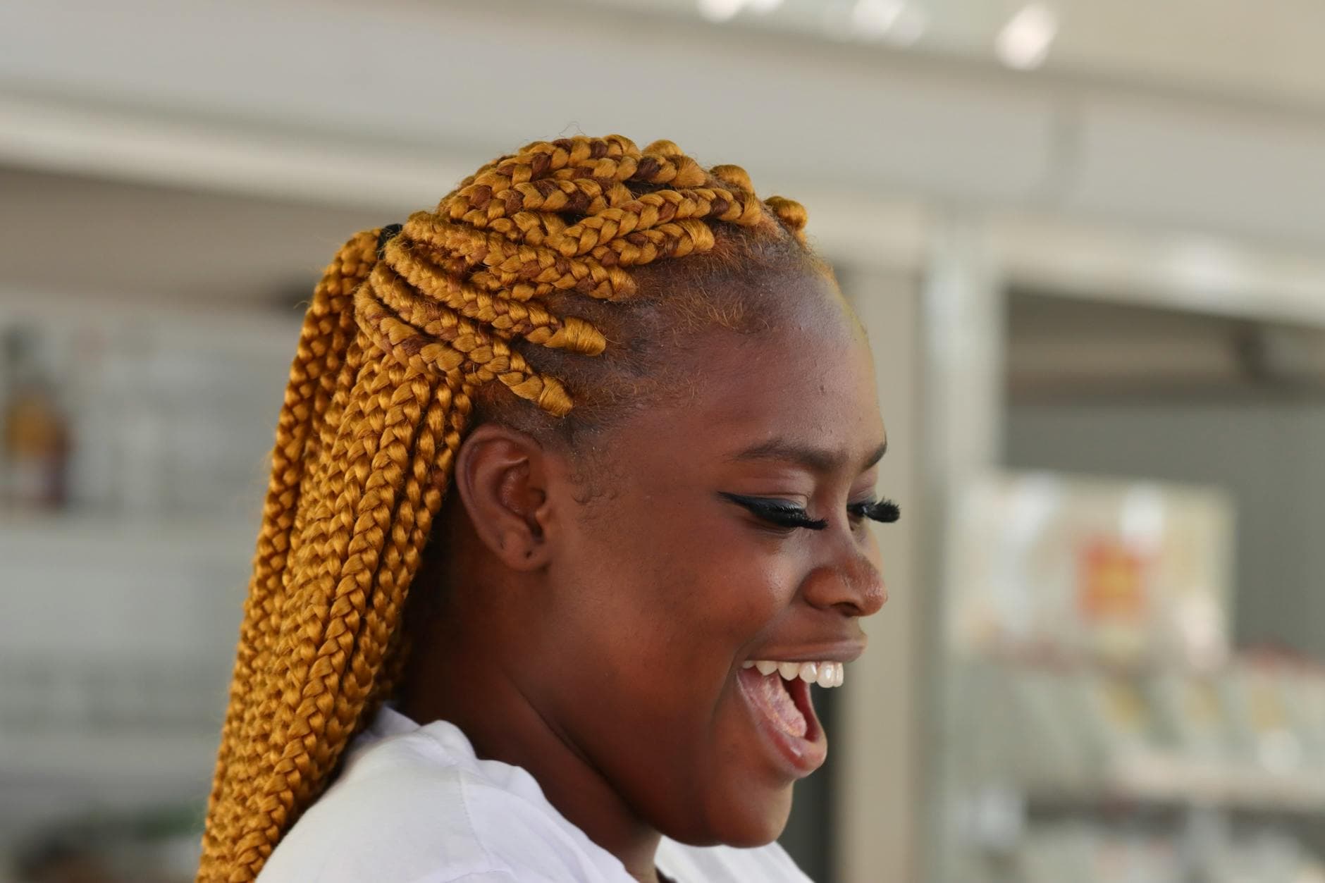 A smiling Black woman with long box braids, showcasing a stylish and vibrant look, standing outdoors in natural light, representing confidence and beauty in protective hairstyles.