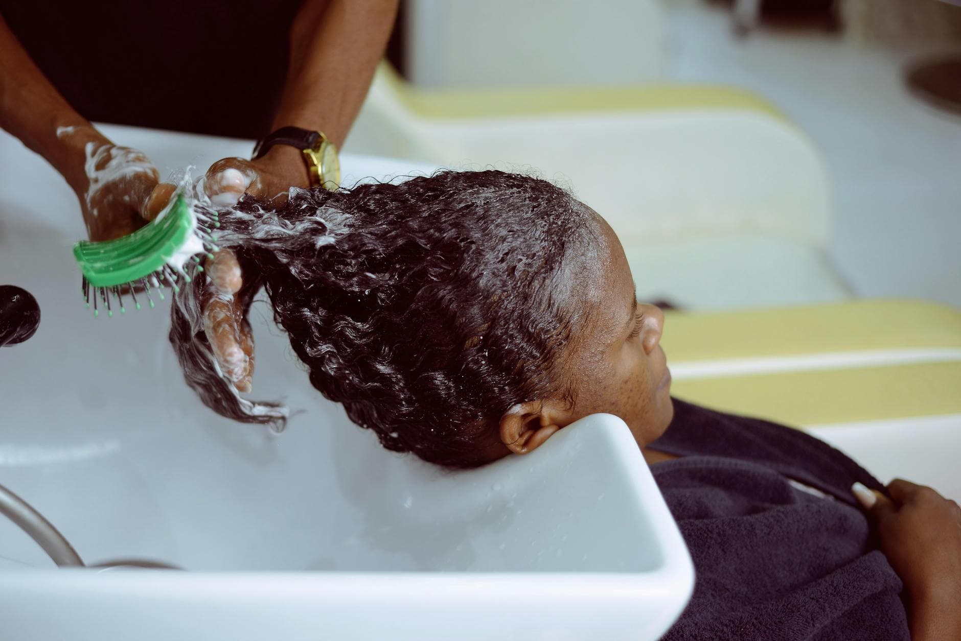 A young Black woman with beautifully textured natural hair, smiling and applying a deep conditioning mask in a bright, well-lit bathroom, showcasing the essence of hair care and hydration.