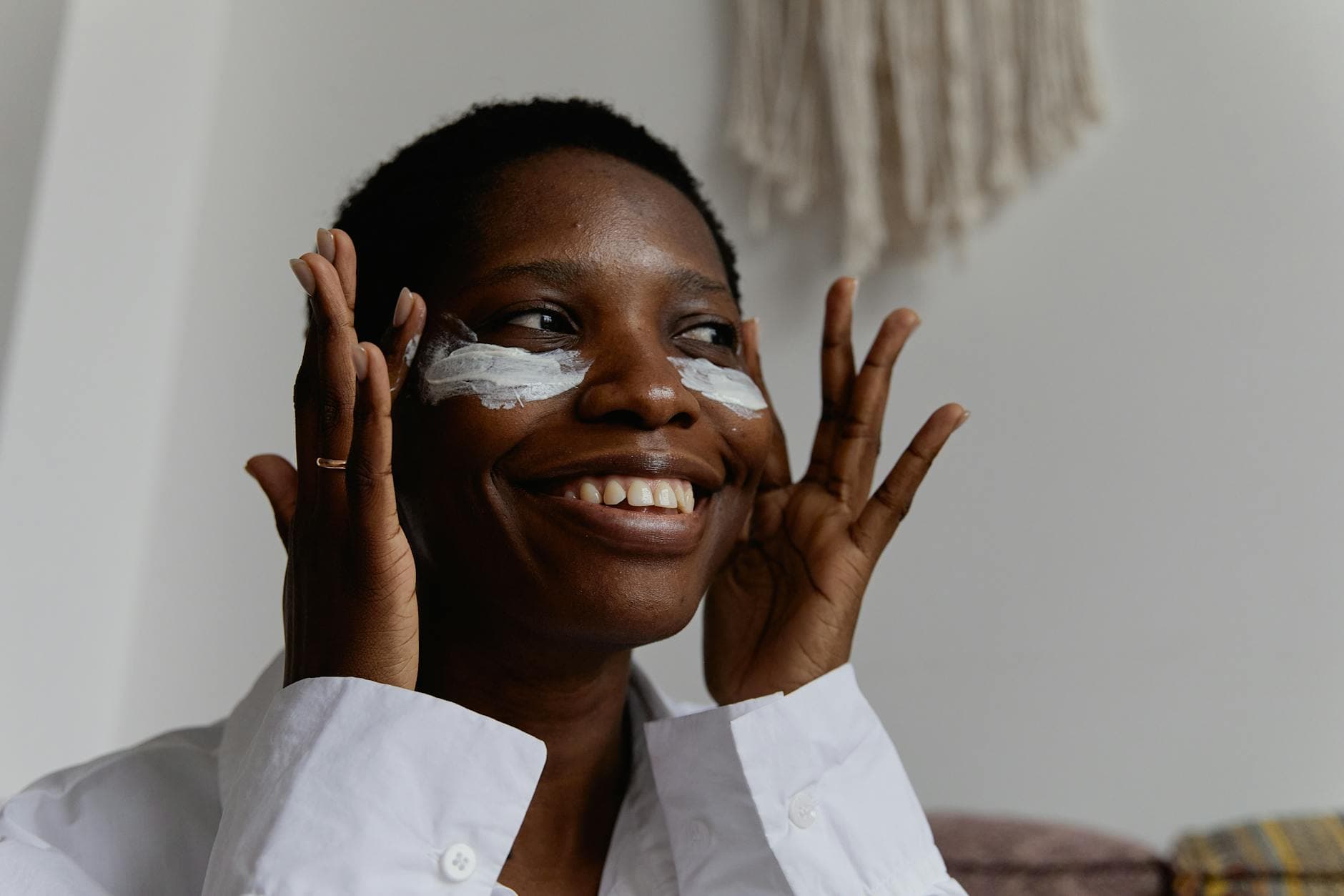 A black woman with textured natural hair applying skincare products, showcasing her radiant skin while smiling confidently in a bright, well-lit environment.
