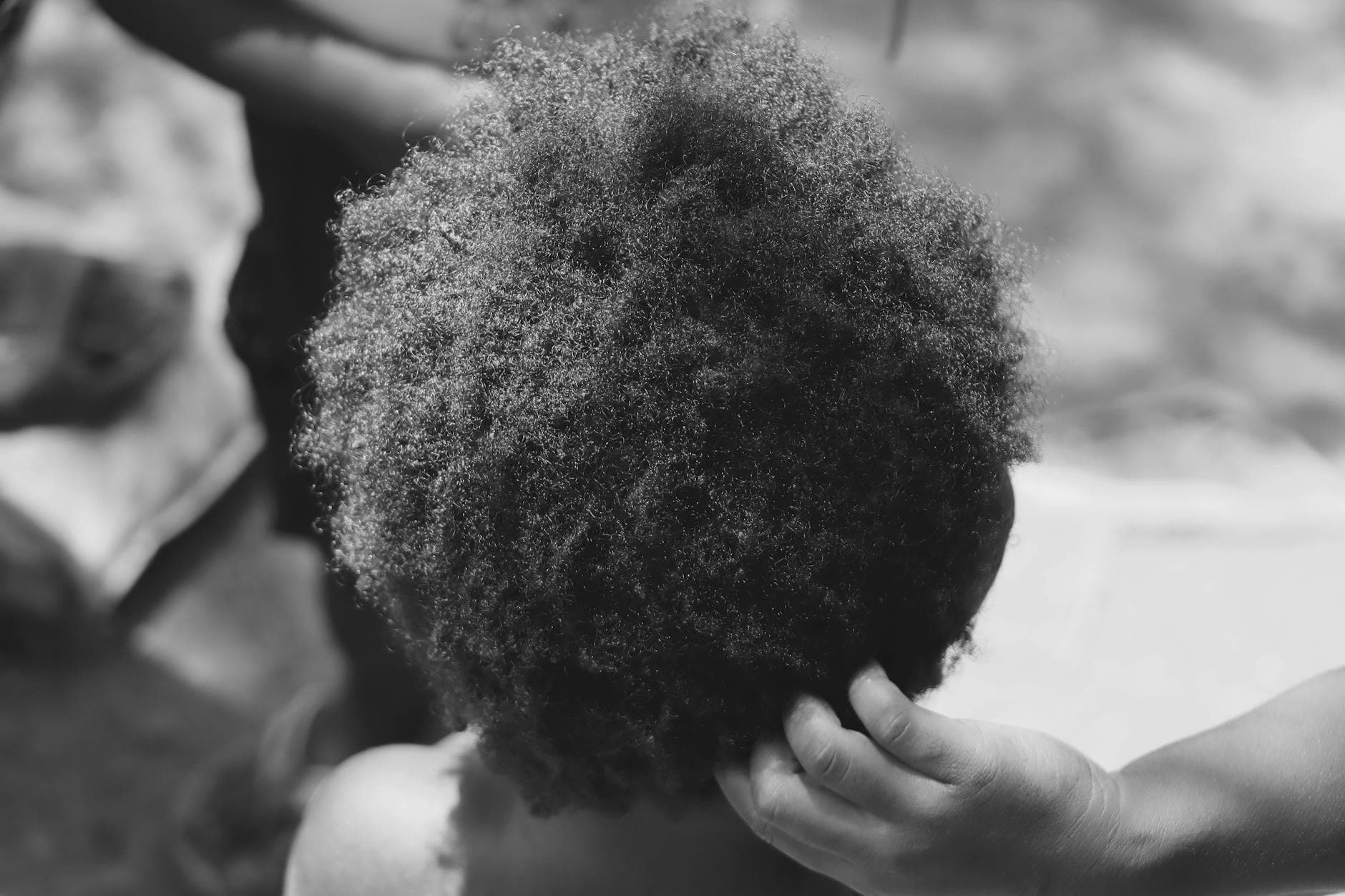 A Black woman with beautifully defined, textured hair applying leave-in conditioner in a bright, well-lit bathroom, showcasing the importance of hair care for textured hair.