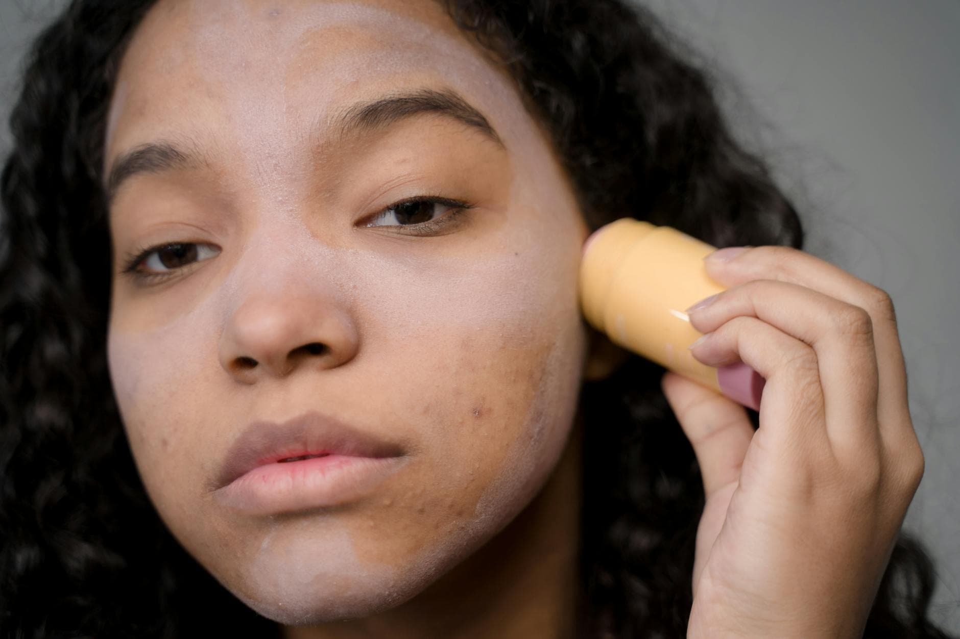 A black woman with textured natural hair applying skincare products to her face in a bright, well-lit setting, showcasing her glowing skin and confidence.